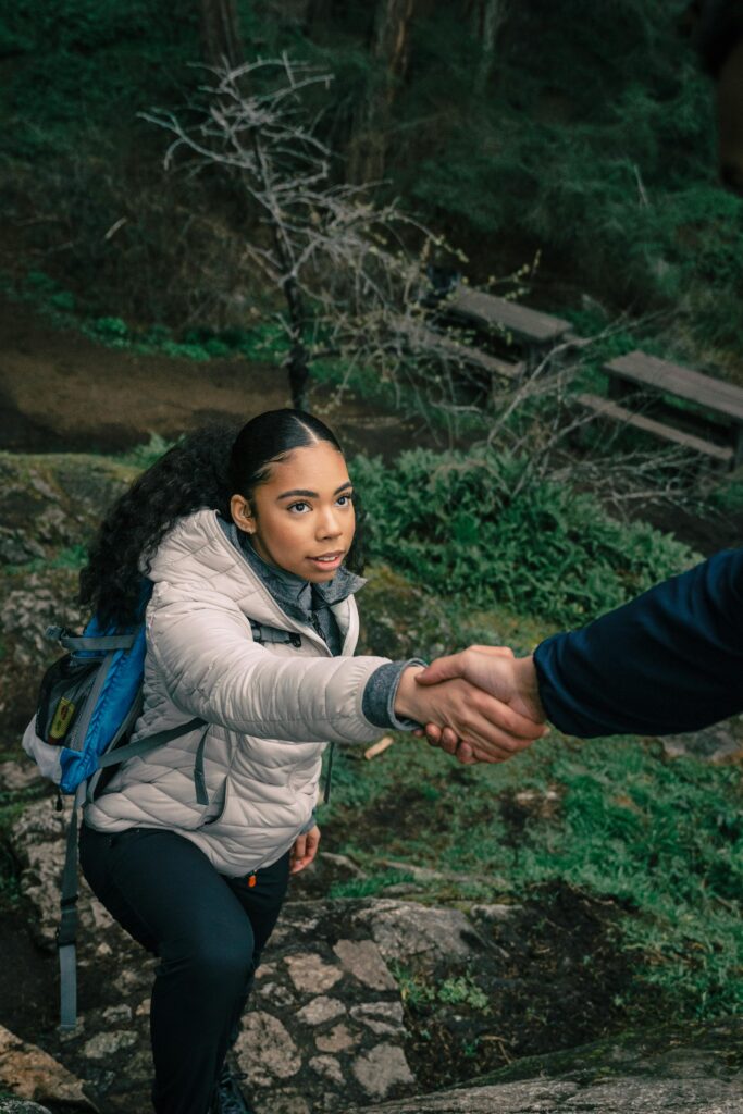 A young black woman receives a helping hand while hiking in a forest.